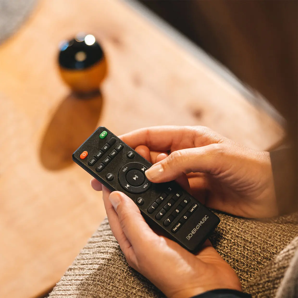 Close-up of hands holding a black TV remote over a beige knitted fabric background.