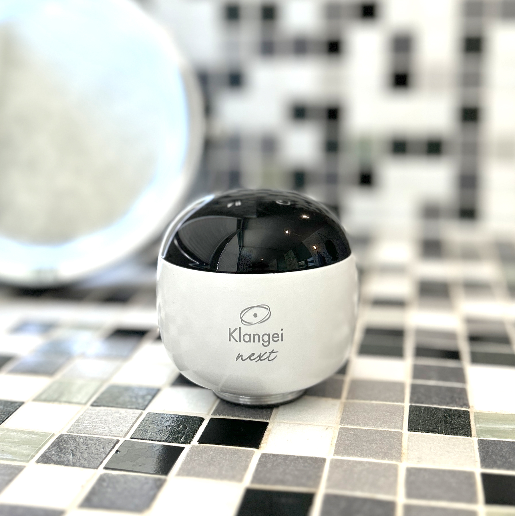 White spherical device with a glossy black top, branded 'Klang ei next' on a tiled surface background.